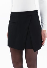 Zwarte mini-jurk met een wikkelontwerp, voorzien van een zijzak en een gladde textuur. Gemaakt van een lichtgewicht stof, geschikt voor verschillende gelegenheden.