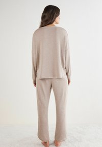 Beige loungedragt bestående af en løst siddende, langærmet top og matchende bukser. Blødt stof med en afslappet silhuet og rundede kanter.