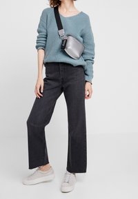 Un maglione lavorato a maglia azzurro chiaro, jeans a gamba larga scuri e sneaker grigio chiaro. Una borsa a tracolla argentata ha una tracolla nera e un logo.