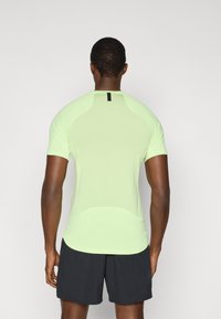 Αθλητική μπλούζα ανοιχτού πράσινου χρώματος με κοντά μανίκια, υφή στο ύφασμα και μίνιμαλ μαύρη ετικέτα στο πίσω μέρος. Συνδυάζεται με σκούρα σορτς.