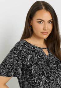 Top nero con un design a contorno floreale bianco, maniche corte e un piccolo dettaglio a chiave sul collo. Tessuto dalla consistenza morbida.