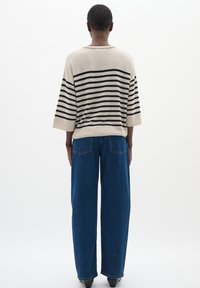 Maglione loose a righe beige e nero con maniche a tre quarti abbinato a jeans scuri blu a vita alta e gamba larga. Tessuto liscio, vestibilità casual.