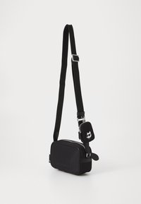 Rectangular black bag made of soft material, featuring a zip closure, adjustable strap, and small attached pouch with a cat design.