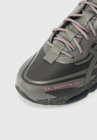Šedá běžecká bota s strukturovaným textilním svrškem, růžovými akcenty a gumovou podešví s tečkovaným detailem. Obsahuje výrazný nápis "GEL-QUANTUM 360".