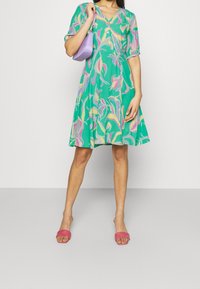 Floral green dress with short sleeves, V-neckline, and pink accents. Paired with pink slide sandals and a small lavender handbag.