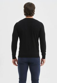 Pull noir à manches longues avec une coupe ajustée et des poignets côtelés, fabriqué dans un matériau doux et texturé, vu de dos.