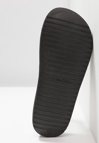 Semelle en caoutchouc noire de chaussure avec des rainures horizontales et le logo Calvin Klein en relief centré.