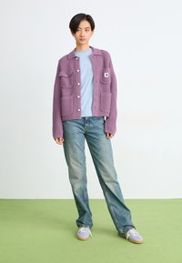 Lila gerippter Cardigan mit aufgesetzten Taschen und Knopfverschluss; hellblaues T-Shirt darunter; lockere Jeans; lavendelfarbene Sneakers.