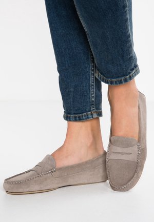 Mocassini in suede grigi con dettagli cuciti, punta arrotondata e design slip-on abbinati a jeans blu risvoltati, che mostrano un look casual.