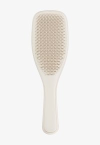 Brosse à cheveux à paddle avec un manche en plastique lisse et crémeux de couleur blanche. La tête de la brosse présente des poils doux à pointes rondes disposés en motif de grille.
