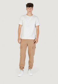 Maglietta in cotone grigio chiaro abbinata a pantaloni cargo beige con tasche laterali, orli affusolati e scarpe da ginnastica bianche. Design semplice e casual.