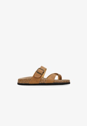 Tan suede sandals with a cork sole, featuring two straps and a side buckle. The design includes a textured insole and black outsole.