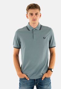 Polo shirt azzurro chiaro con colletto e polsini a righe bianche e nere, dotato di un'apertura con due bottoni e un piccolo logo sul lato sinistro del petto.