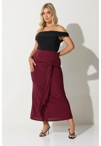 Svart off-the-shoulder topp i kombination med en vinröd omlottkjol med en knutdetalj i midjan, tillverkad av mjukt och slätt tyg.