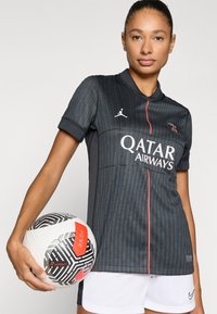 Must vertikaalsete triipudega särk kraega, millel on Jordan'i logo ja Qatar Airwaysi bränding. Hoides musta ja valget mustriga jalgpalli.