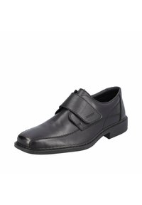 Chaussure en cuir noir avec un bout arrondi, dotée d'une large sangle Velcro et de détails de coutures discrets le long de la tige et de la semelle.