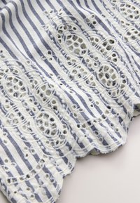 Tissu blanc avec des rayures verticales bleu marine et des détails en dentelle brodée formant des motifs circulaires et des bords festonnés.