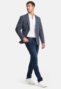 Men's casual outfit featuring a blue blazer, white shirt, and dark blue skinny jeans, paired with white sneakers. Smooth fabric, tailored fit.