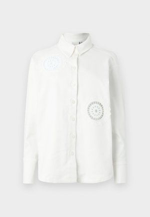 Bela srajca z gumbki in dolgimi rokavi, z dvema vezenima dekorativnima vzorama in klasičnim ovratnikom. Mehka, teksturirana tkanina.
