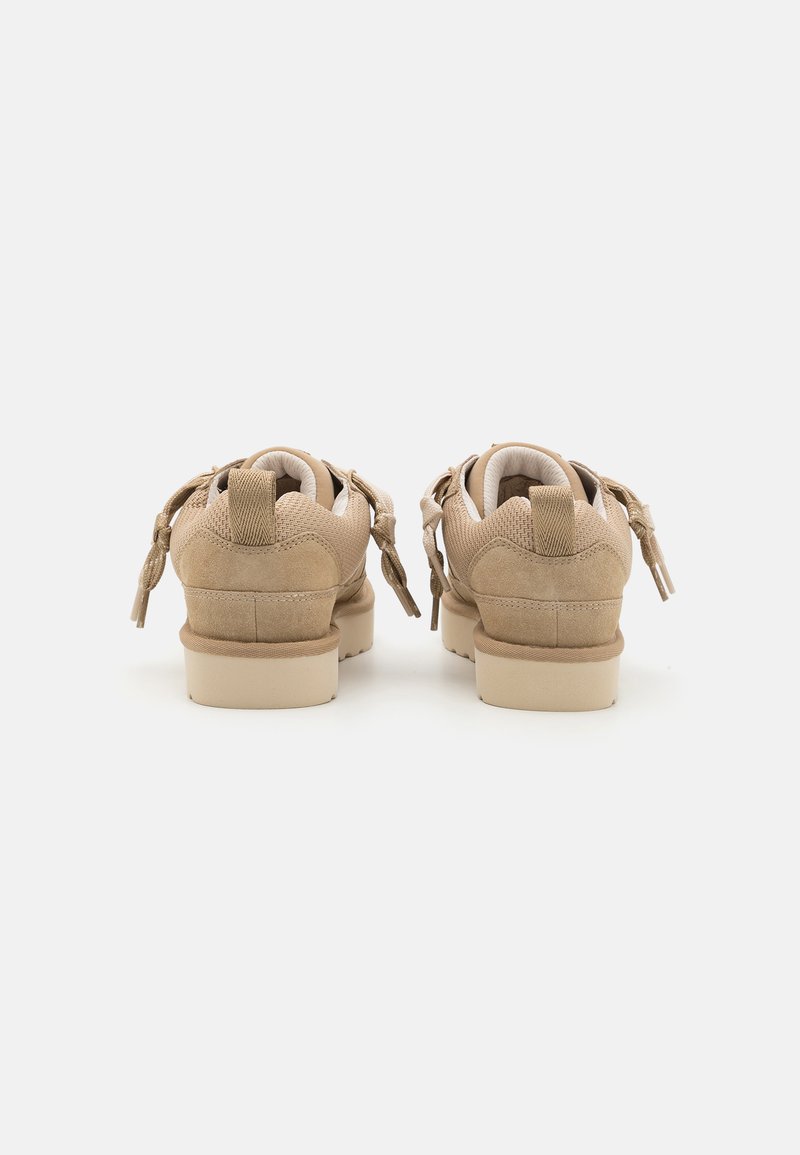 Beige Sneaker mit einer Kombination aus Mesh und Veloursleder, niedrigem Profil, Schnürung und Riemendetail sowie Gummisohle. Die Rückansicht zeigt einen gepolsterten Schaft.