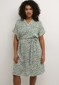 Vestido de manga corta con escote en V, base blanca y patrones abstractos en verde. Presenta una cintura anudada y una silueta fluida. Tejido suave.