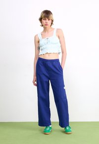 Top cropped azul claro com alças largas e laço à frente; calças cargo soltas de corte largo em azul-marinho com bolsos laterais; sapatilhas verdes.