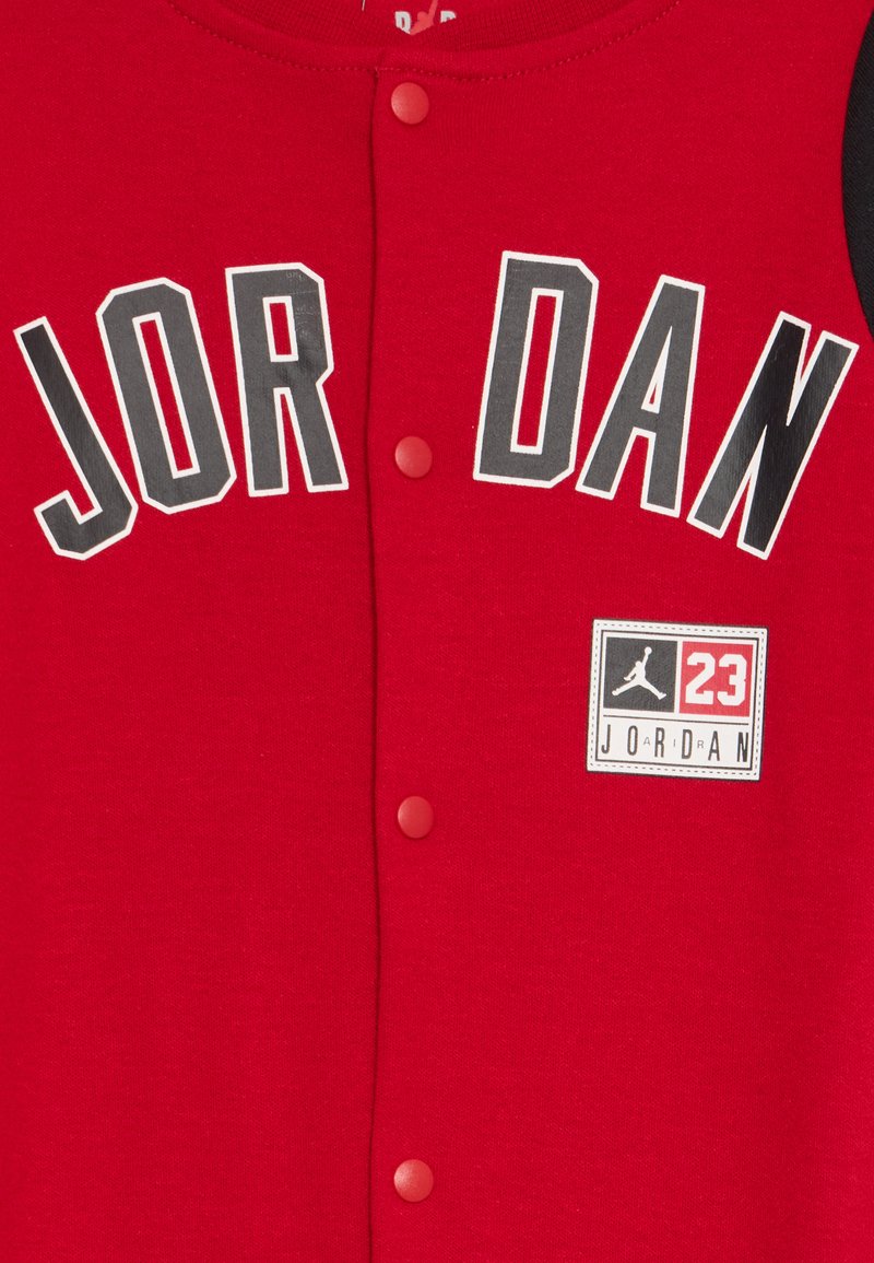 Rote Baumwollweste mit Druckknöpfen, die mit "JOR DAN" Schriftzug und einem quadratischen Logo mit "23" in Schwarz-, Weiß- und Grautönen versehen ist.