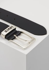 Ceinture en cuir noir avec une boucle métallique argentée rectangulaire, arborant le logo "Levi's". Texture lisse et plusieurs trous de réglage visibles.