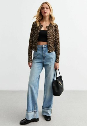 Giacca cropped leopardata, top corto nero, jeans a gamba larga blu chiaro, mocassini neri e una borsa nera con hardware dorato.