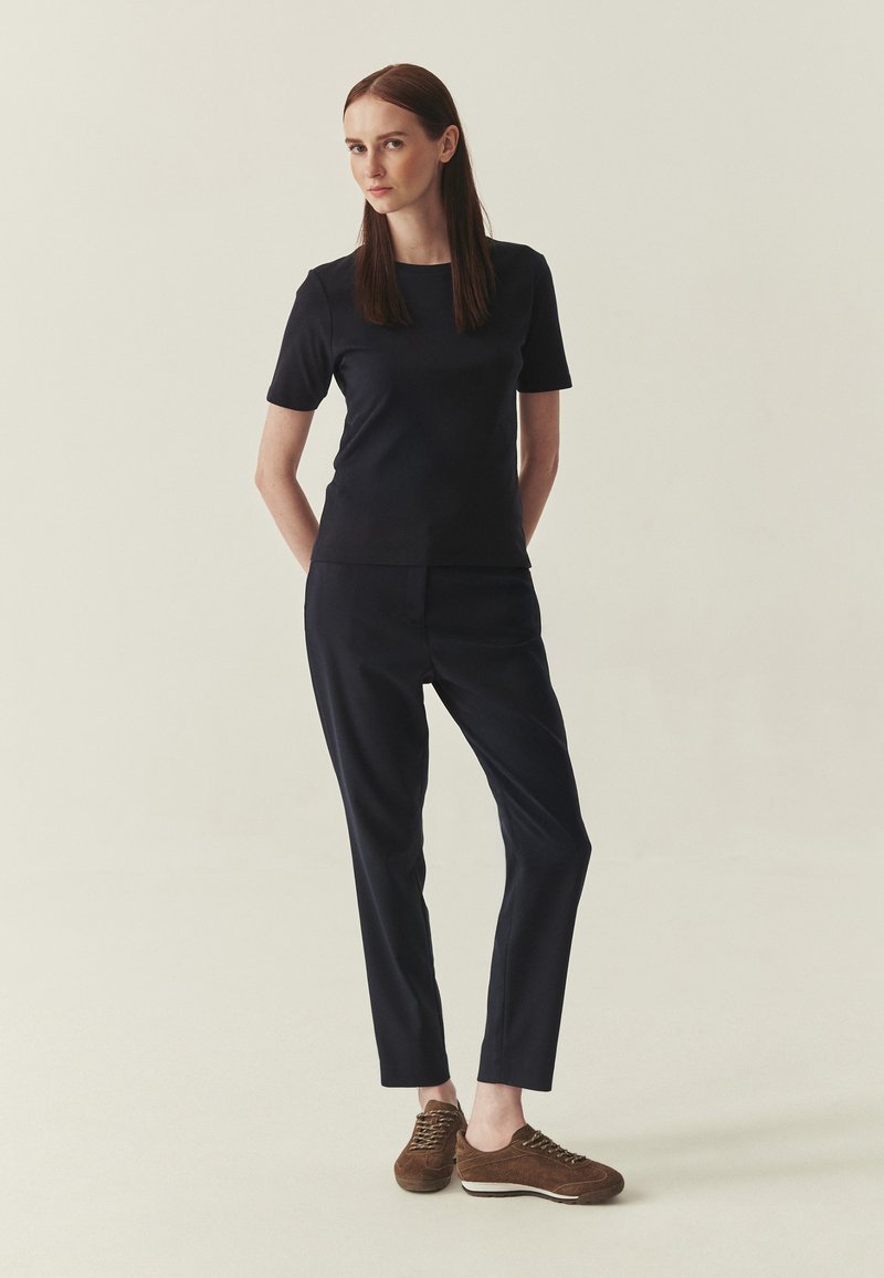 Haut bleu marine à manches courtes et pantalon ajusté, assortis à des baskets en daim marron. Design simple avec une texture lisse, créant un look harmonieux.