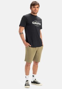 Black short-sleeve t-shirt with "Quiksilver" print, olive green shorts, black sneakers with white laces, and white ankle socks.