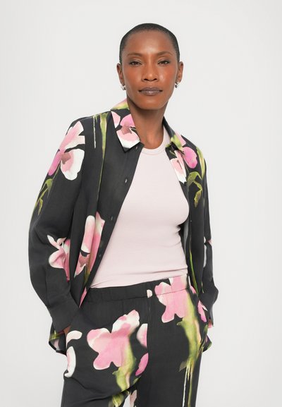 Black floral shirt featuring pink and green flower patterns, worn over a light pink top. The shirt has a relaxed fit and button closure.