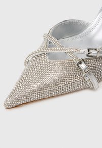 Sudraba purngalvju papēži ar rotājošām rhinestones, ar pārklātiem siksnām un metālisku iekšējo apdari. Gluda tekstūra un mirdzoša virsma.