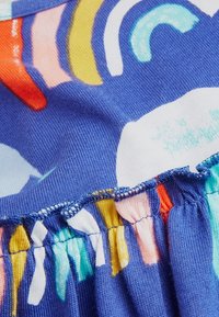 Teksturowana niebieska tkanina z kolorowymi abstrakcyjnymi wzorami w odcieniach pomarańczowego, żółtego, różowego i białego. Zgromadzony detal szwu na krawędzi.