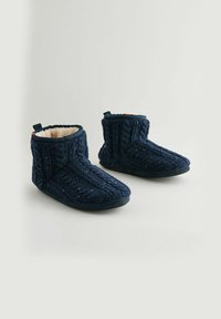 Zapatillas de punto en color marino con un diseño texturizado, forro de piel sintética y puntera redondeada. Incluyen una pequeña pestaña en la parte trasera para facilitar el uso. Suela plana negra.