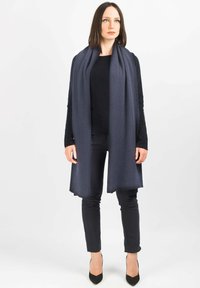 Sciarpa di lana blu scuro drappeggiata sulle spalle, con una texture liscia e bordi frangiati. Indossata con un top nero e pantaloni slim fit.