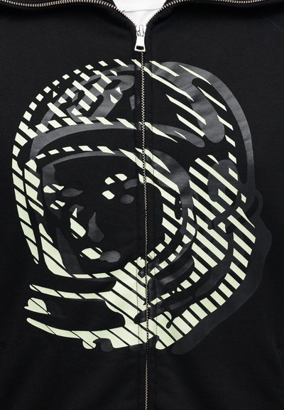 Μαύρο φούτερ με φερμουάρ, στολισμένο με αντανακλαστικό γραφικό αστροναύτη, με έντονες ρίγες και απαλή υφή, τονίζοντα ς κυρίαρχα τα σχεδιαστικά στοιχεία.