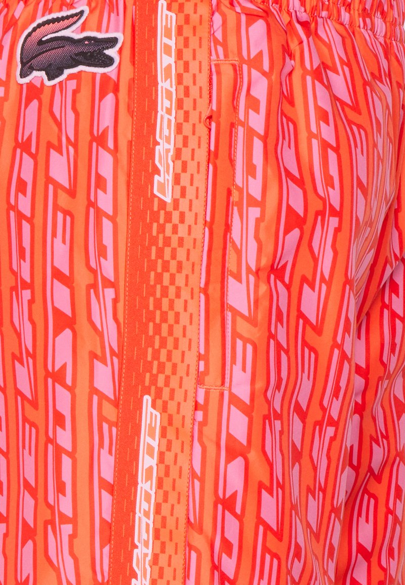 Bañadores naranjas con un parche de logo, patrón geométrico y rayas laterales en contraste. Fabricados con un tejido ligero y con cintura elástica.