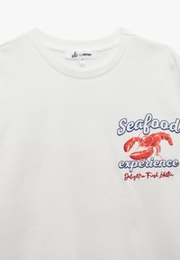 Hvid bomulds t-shirt med et farverigt hummergrafik. Teksten siger "Sømadoplevelse" og "Dejlig frisk hummer" i blå og rød.