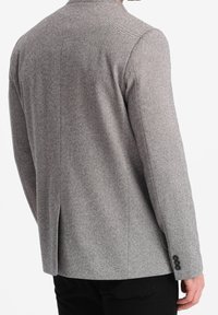 Blazer grigio a motivo herringbone con forma aderente, spacchetto singolo sul retro e dettagli in bottone nero sui polsini. Tessuto testurizzato.