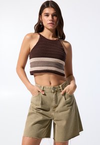 Ruskea ja beige raidoitettu virkattu crop-top, jossa on halterneck-muotoilu, yhdistettynä khaki-denim-shorteihin, joissa on taskut ja revitty helma.