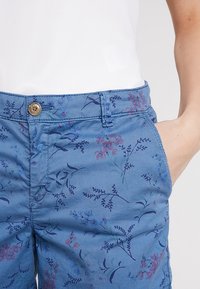 Pantalon bleu à motif floral en coton, avec une fermeture avant à boutons, des poches latérales et une texture lisse.