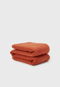 Deux écharpes en laine orange rouille soigneusement pliées, empilées sur un fond gris clair uni.