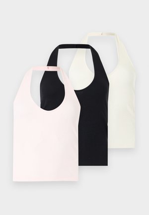 Jeune femme debout portant un haut blanc sans manches, un jean bleu ample avec les ourlets retroussés et des sandales noires sur fond blanc uni.