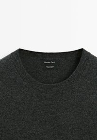 Maglione in cashmere grigio scuro con scollatura rotonda, rifiniture a coste e un'etichetta che mostra il nome del marchio e le informazioni sul materiale.