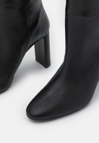 Bottines en cuir noir avec un design à bout pointu, dotées d'un talon épais et haut et d'une texture lisse. Aucuns motifs ni accents visibles.