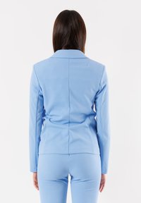 Blazer azzurro chiaro realizzato in tessuto liscio, con colletto classico e design aderente. Retro sagomato con cuciture per forma e struttura.