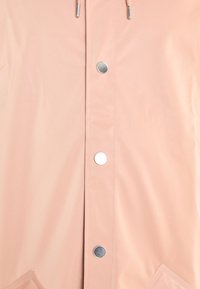 Light pink rain jacket featuring a smooth, glossy texture, silver snap buttons, and a pocket on the front. Drawstrings visible at the collar.