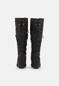 Bottes noires montant jusqu'au genou en daim souple, avec un design froncé, une fermeture à lacets avec œillets dorés et une semelle plate en caoutchouc.