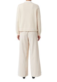 Felpa color crema e pantaloni larghi abbinati, realizzati in tessuto morbido, con polsini e vita a costine, linee pulite e design minimal.